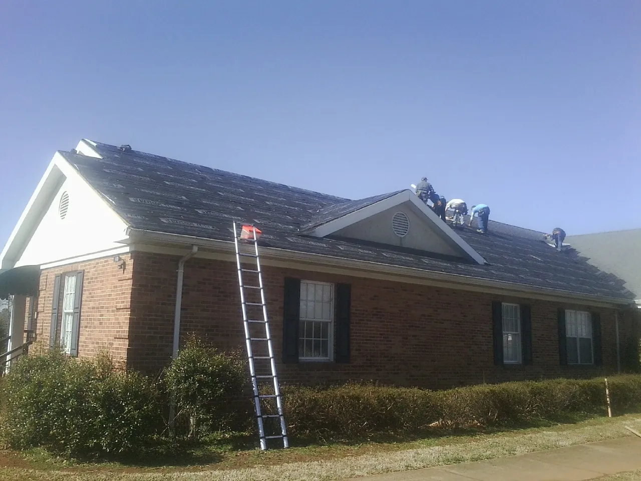 Crew tearing shingles off a brick ranch roof with a ladder set — Emergency Roof Repair work by our crew in Lenhartsville