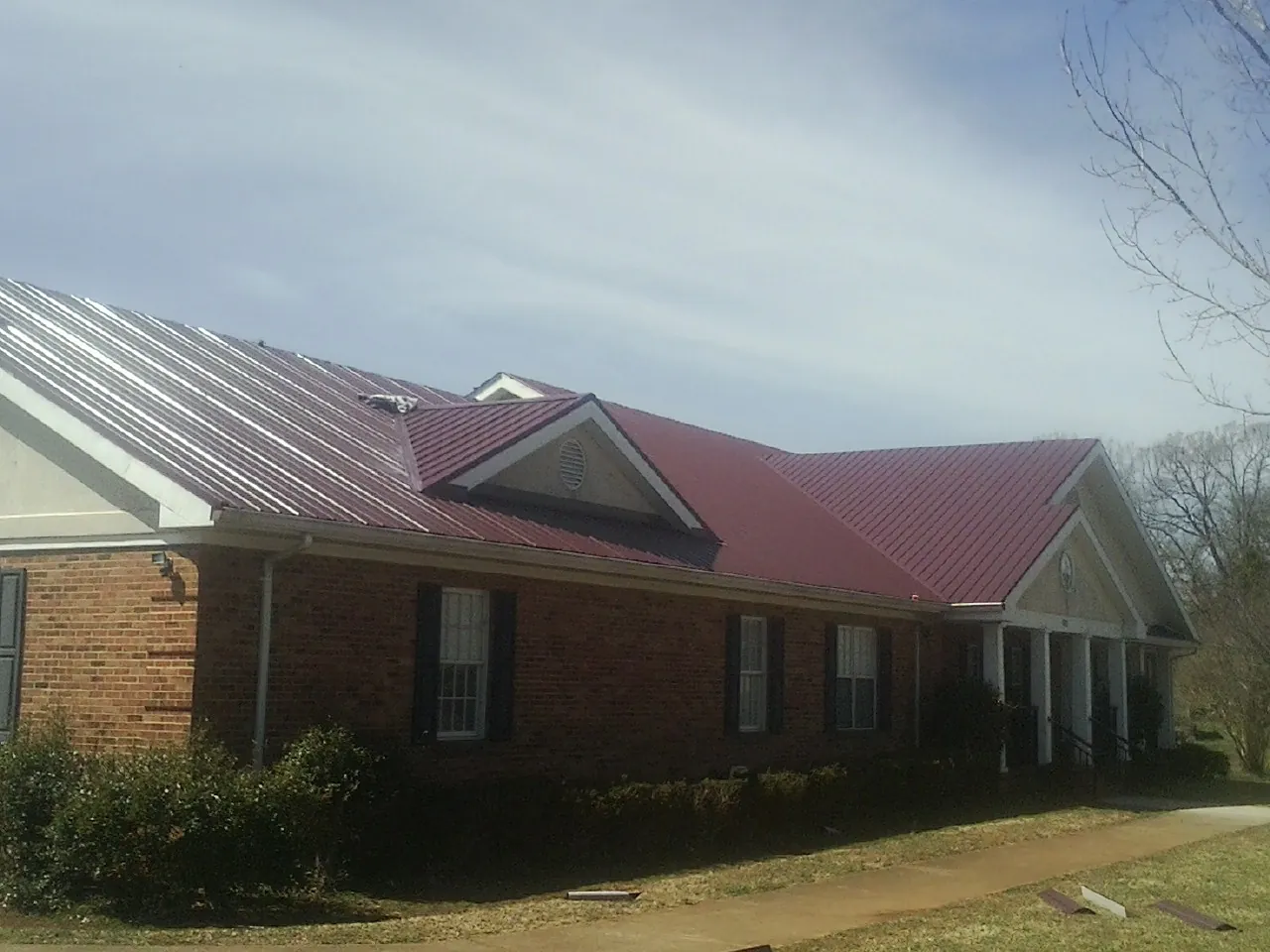 Red metal roof with gabled entries on a long brick building, from a Hail Damage Roof Repair job in Lenhartsville