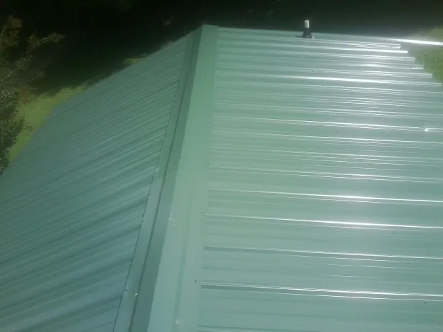 New green metal panels meeting at the ridge of a roof — Flat Roof Repair work by our crew in Lenhartsville