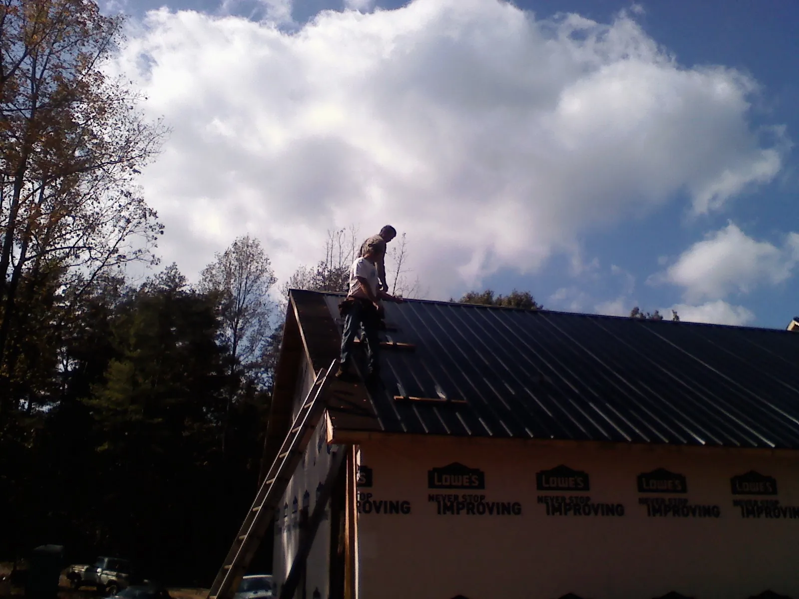 Roofer fastening dark metal panels high against a cloudy sky, from a Roof Inspection job in Lenhartsville