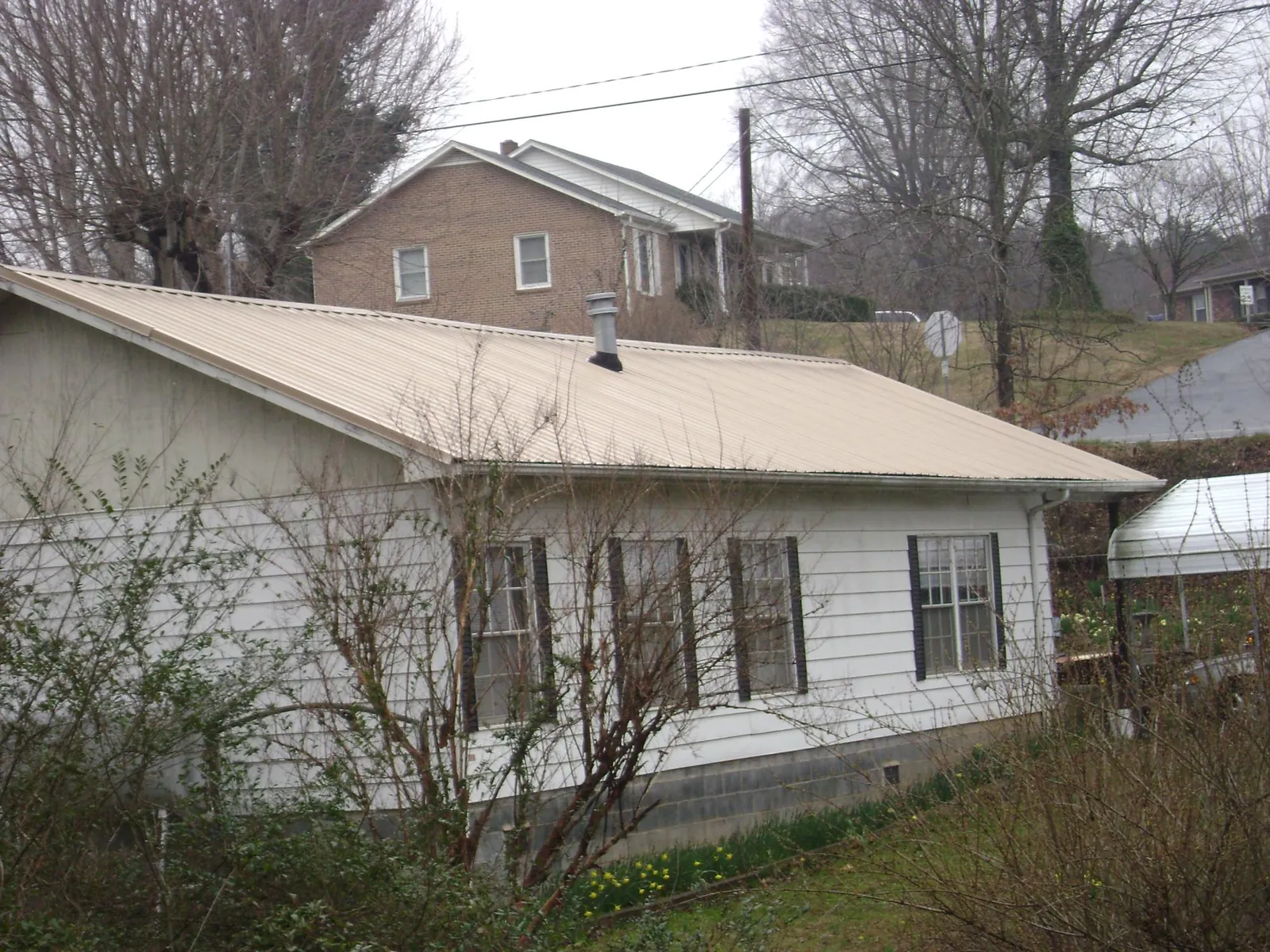 Tan metal roof on a white sided house set into a hillside — Commercial Roofing by Roofing Brothers in Lenhartsville